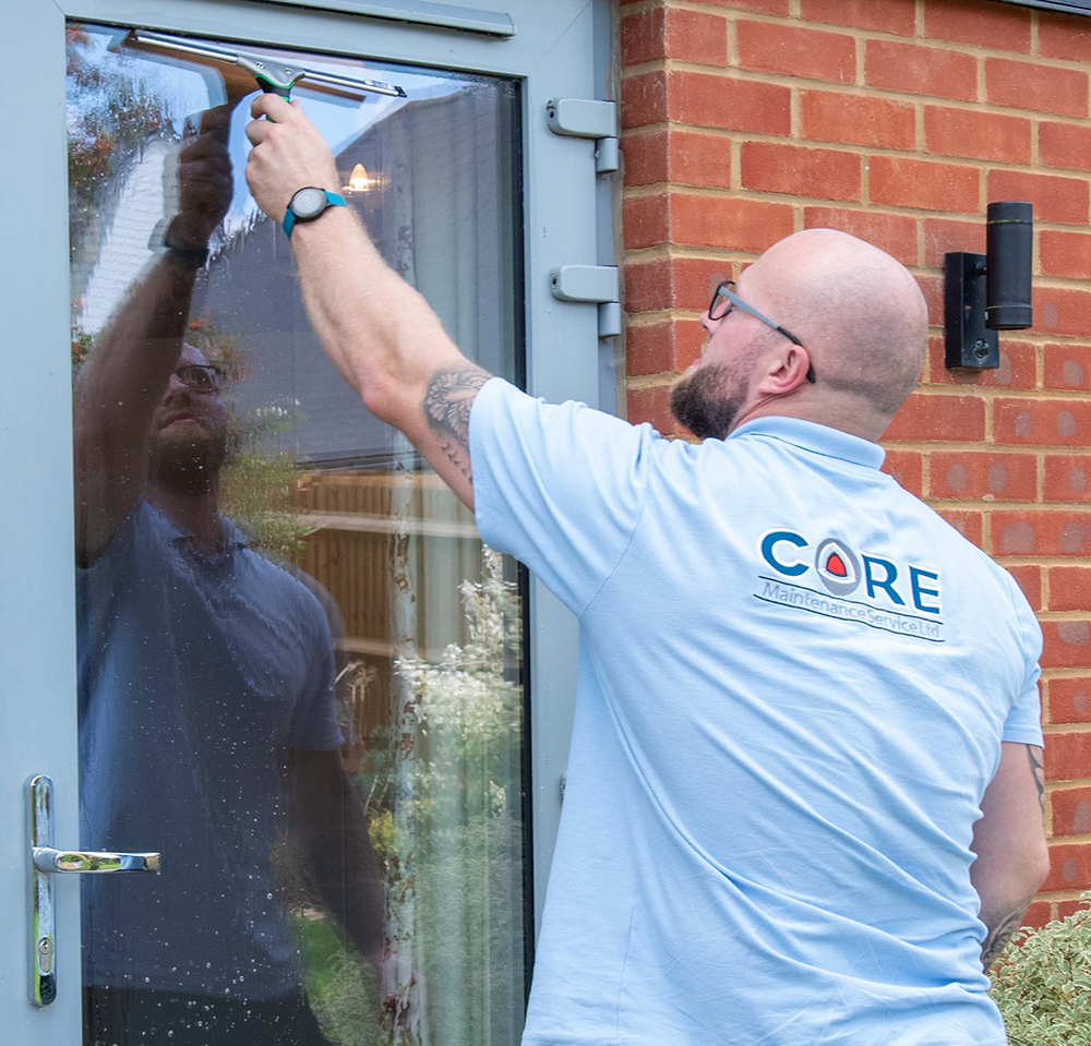 Male wearing pale blue Core shirt using a squeegee to clean a glass door