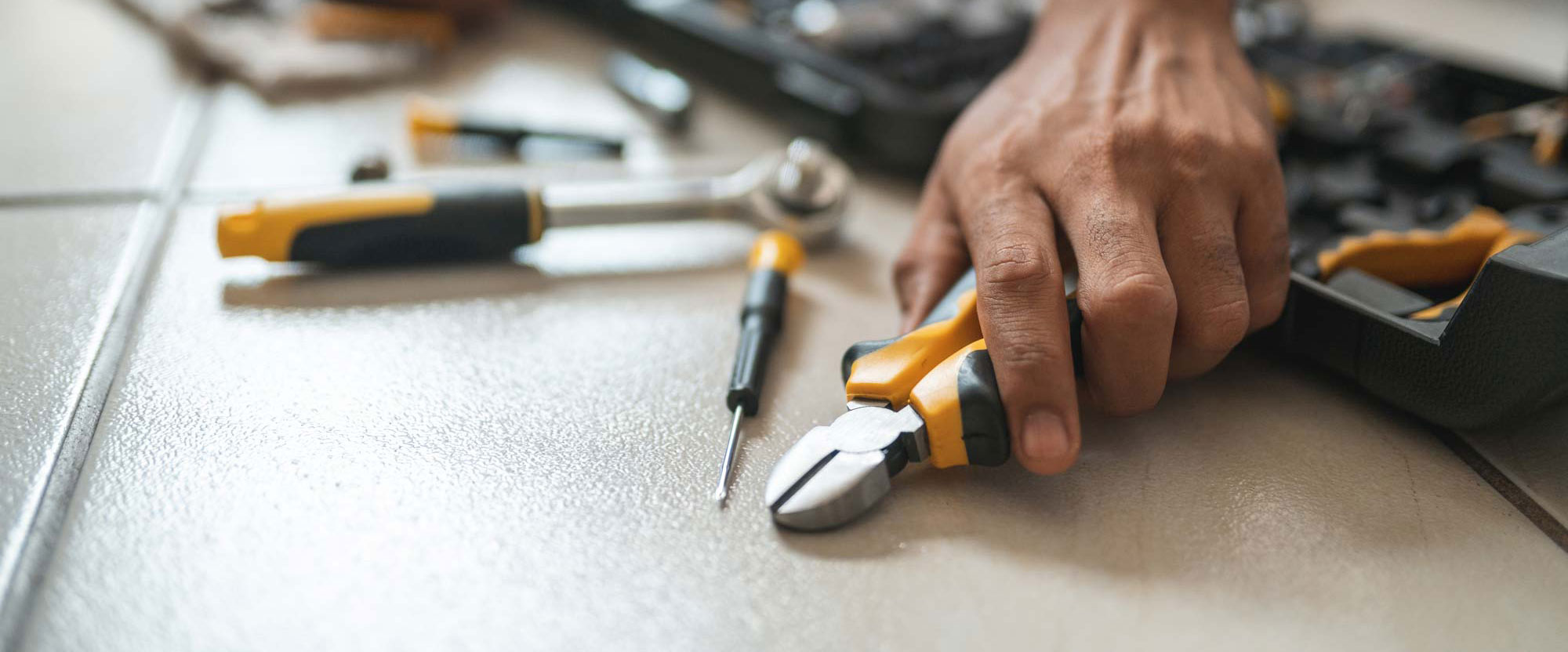 A workmans hands picking up a pair of pliers